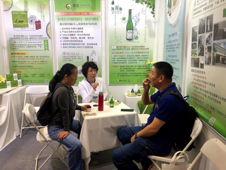 工作人員在洽談桌用小湯匙向兩位來賓解說檸檬酵素