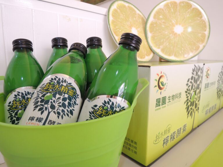 綠水精靈檸檬酵素瓶裝在綠色提籃中，旁邊是晟園禮盒與檸檬切片擺飾
