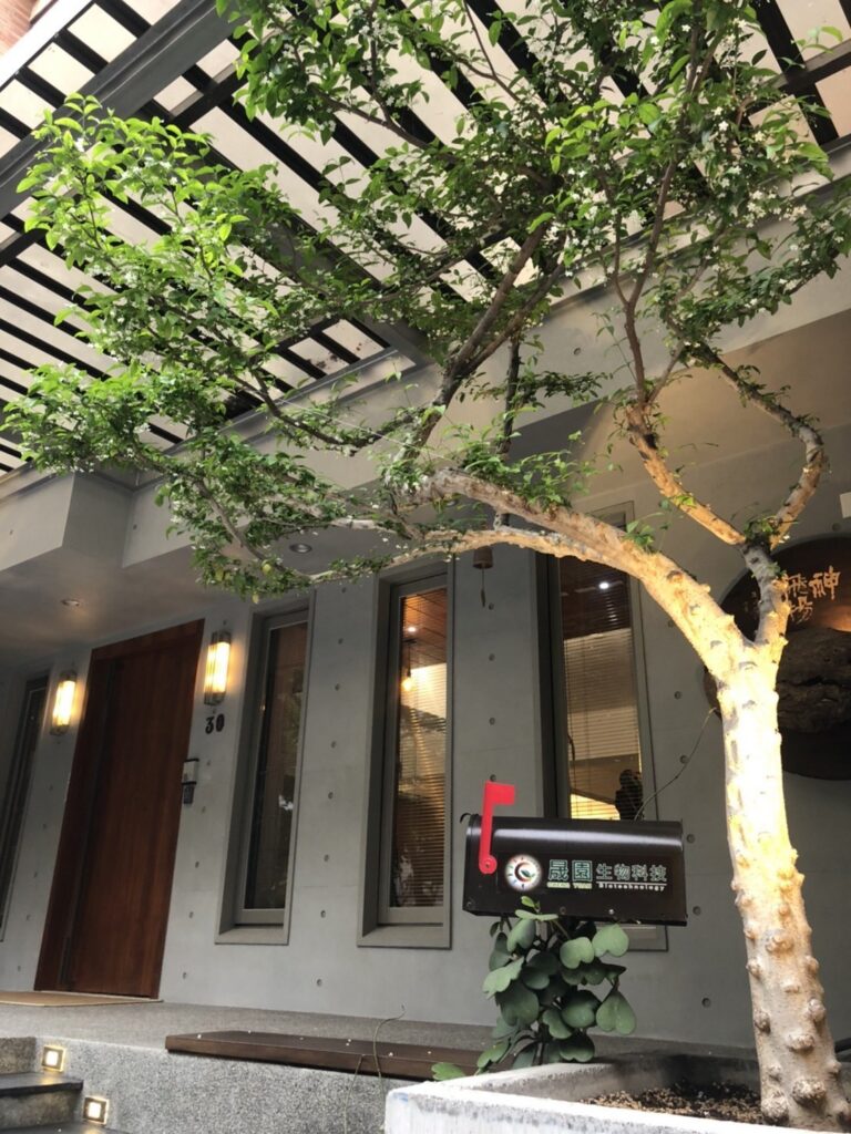 晟園高雄公司門口，綠樹罩著木格柵屋簷與品牌信箱