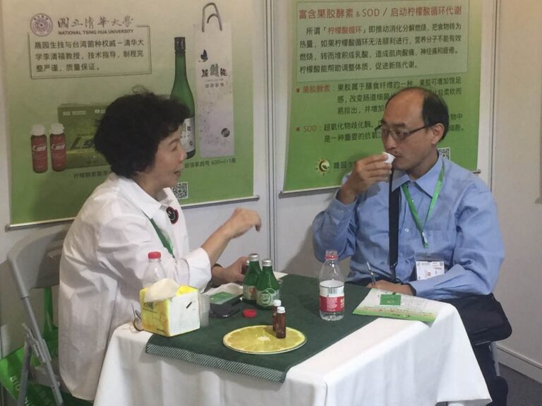 2019 上海國際酵素產業博覽會：螢綠制服成員手持綠色資料夾向訪客解說，背景 L99 七大承諾看板